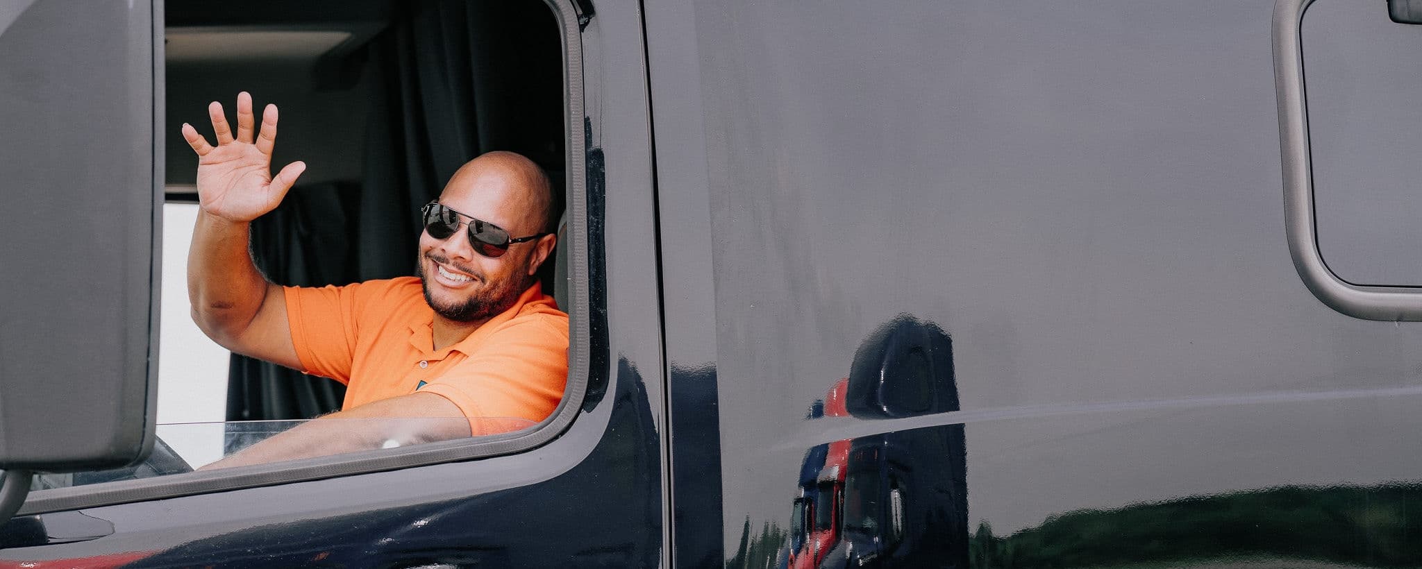An EOS driver smiling and waving from the cab of his truck