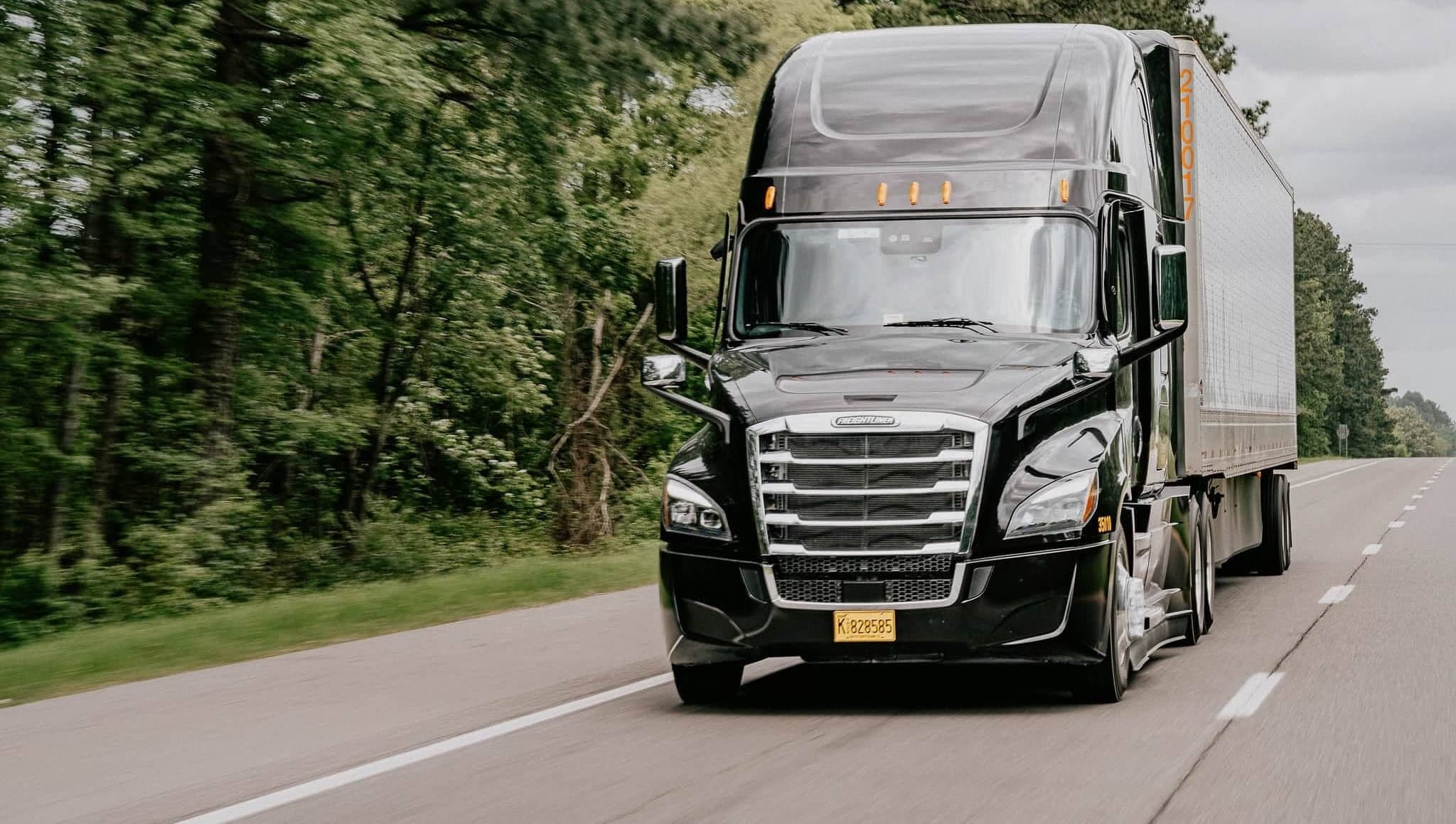 A black EOS Trucking Freightliner pulling a trailer down a tree-lined highway